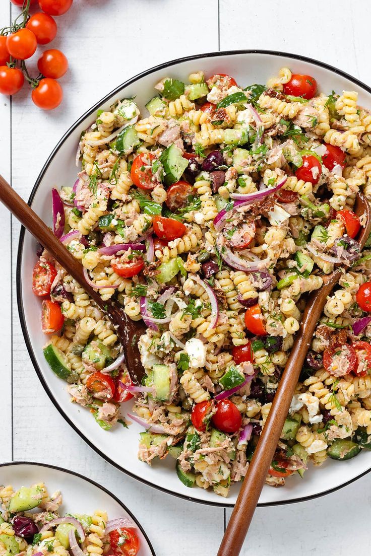 two plates filled with pasta salad on top of a white table next to cherry tomatoes