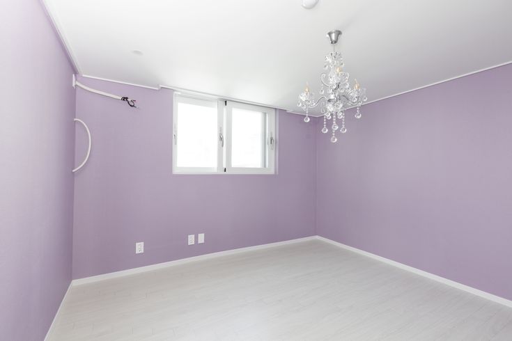 an empty room with purple walls and chandelier hanging from the ceiling in front of a window