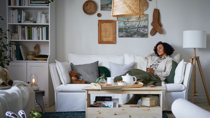 a woman sitting on a couch in a living room next to a coffee table and bookshelf