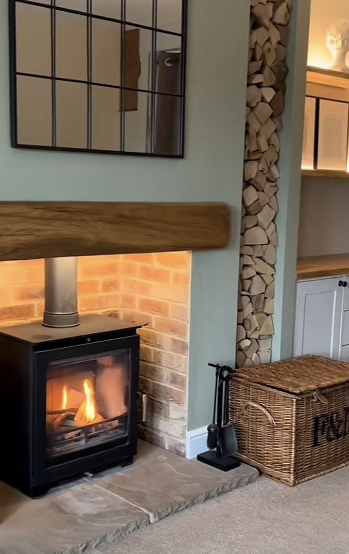 a wood burning stove in a living room next to a basket with logs on it