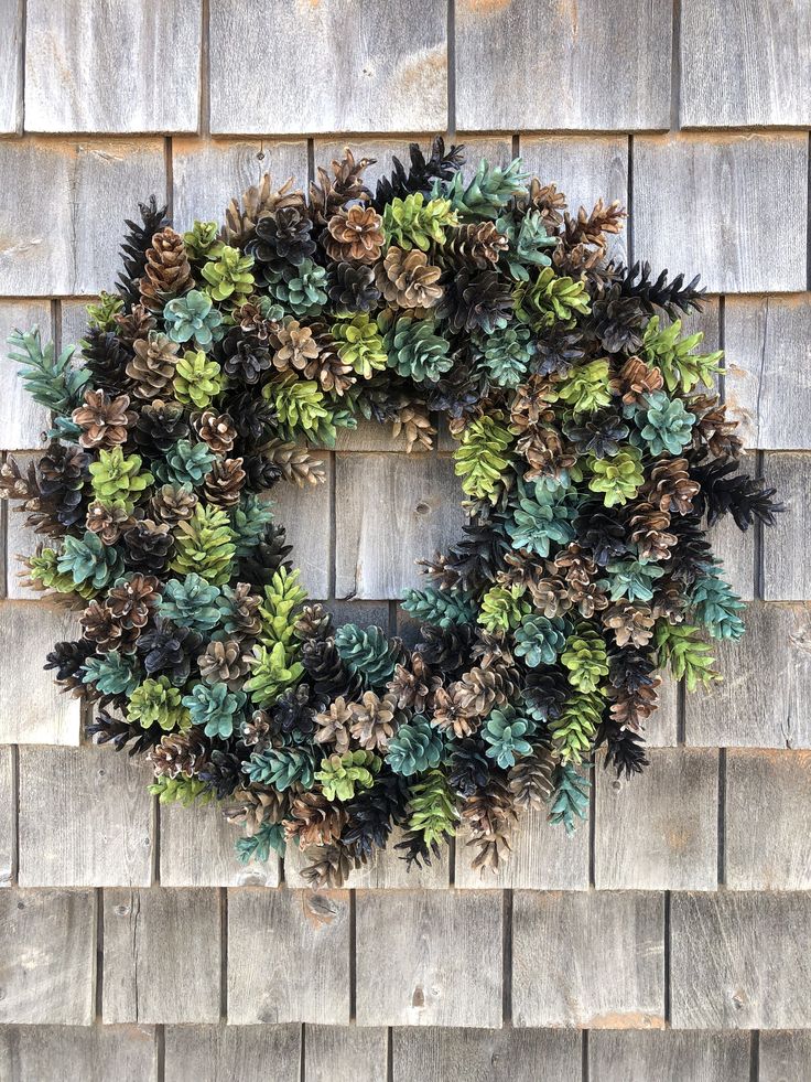 a wreath made out of pine cones and green leaves on a wooden wall with wood planks in the background