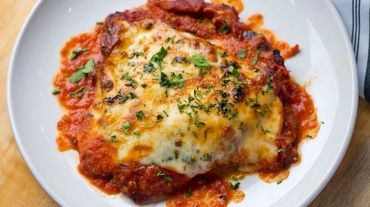 a white plate topped with lasagna covered in marinara sauce and parmesan cheese