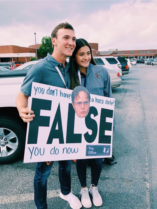 a man and woman standing in front of a car holding a sign that says false