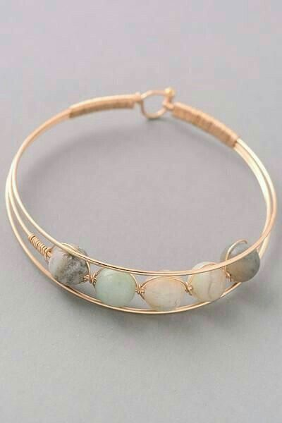 a gold bracelet with white and green stones on it's side, sitting on a gray surface