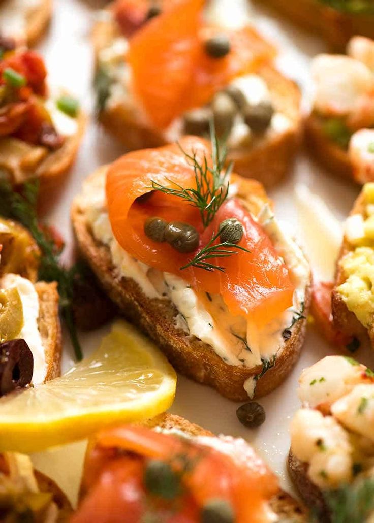 small pieces of bread with different types of food on them and lemon wedges next to each other