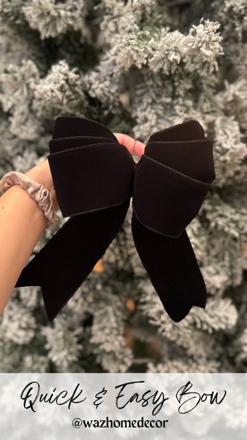 a hand holding two black bows in front of a christmas tree