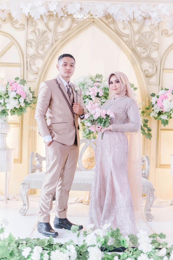 a man and woman standing next to each other in front of a floral arch with flowers