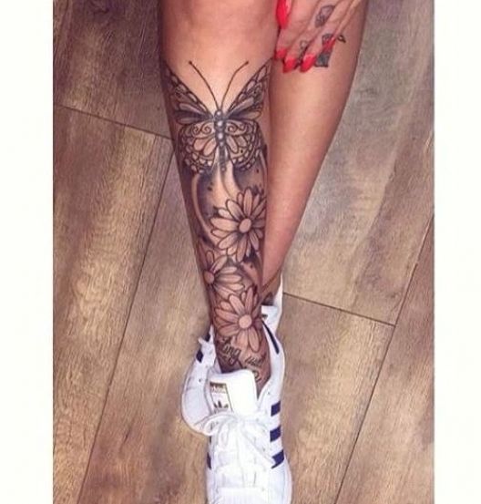 a woman's leg with tattoos on it and flowers in the bottom right corner