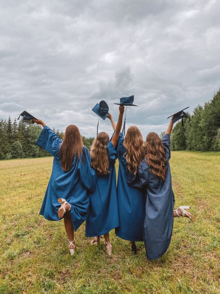 three girls in blue graduation gowns and caps are holding their hands up to the sky