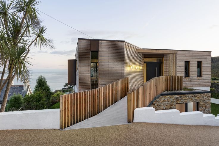 a modern house with wood siding and stone steps leading up to the front door, overlooking the ocean