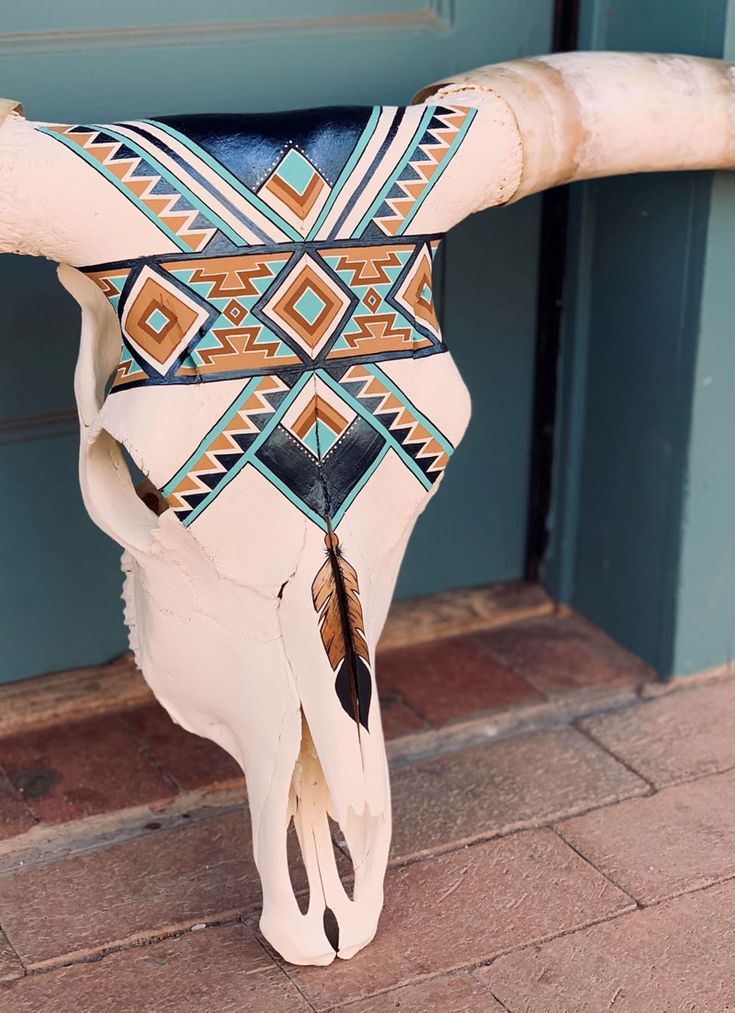 a cow's skull is decorated with native american patterns and feathers on the side of a door