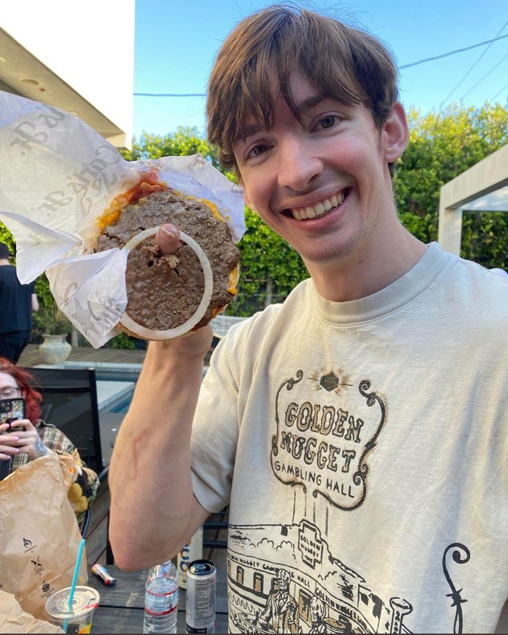 a young man holding up a sandwich in front of him and smiling at the camera