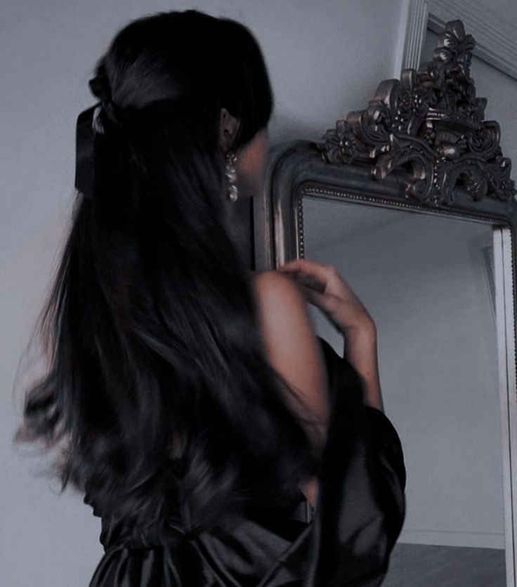 a woman with long hair looking at herself in the mirror and holding her hand on her hip