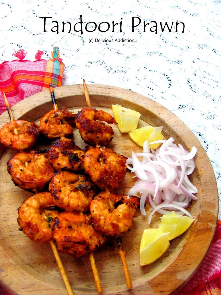 a wooden plate topped with grilled shrimp next to lemon wedges and onions on skewers