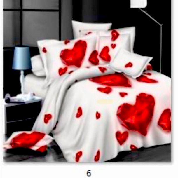 a bed with red hearts on it and white sheets in the middle, next to a lamp