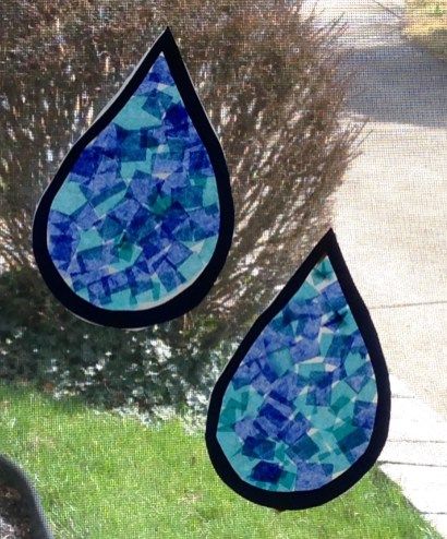 two stained glass drops hanging from the side of a window in front of a tree