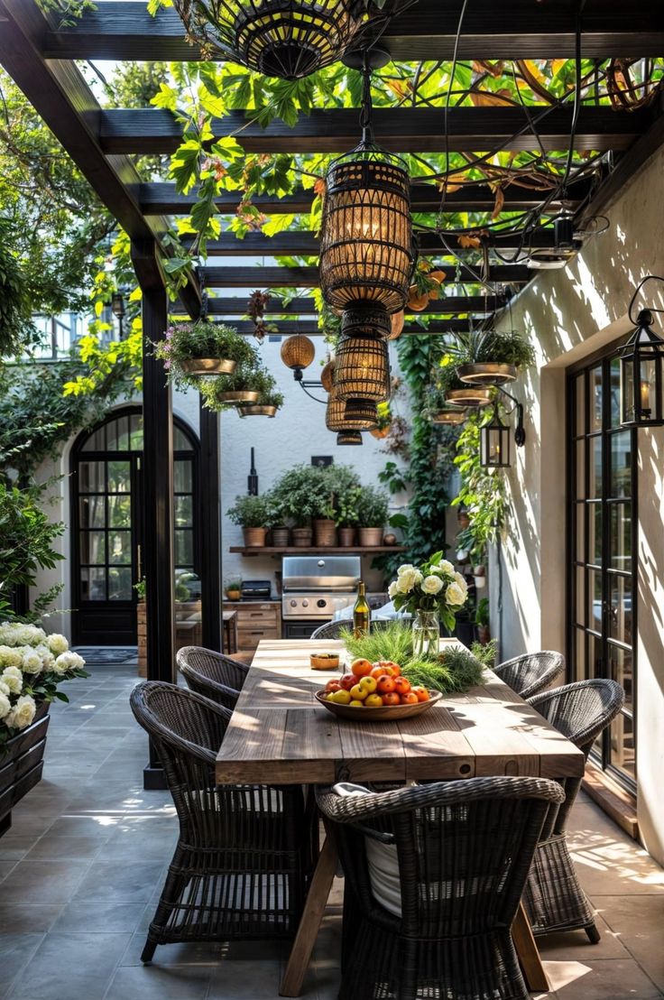 an outdoor dining area with potted plants on the table and hanging lights above it