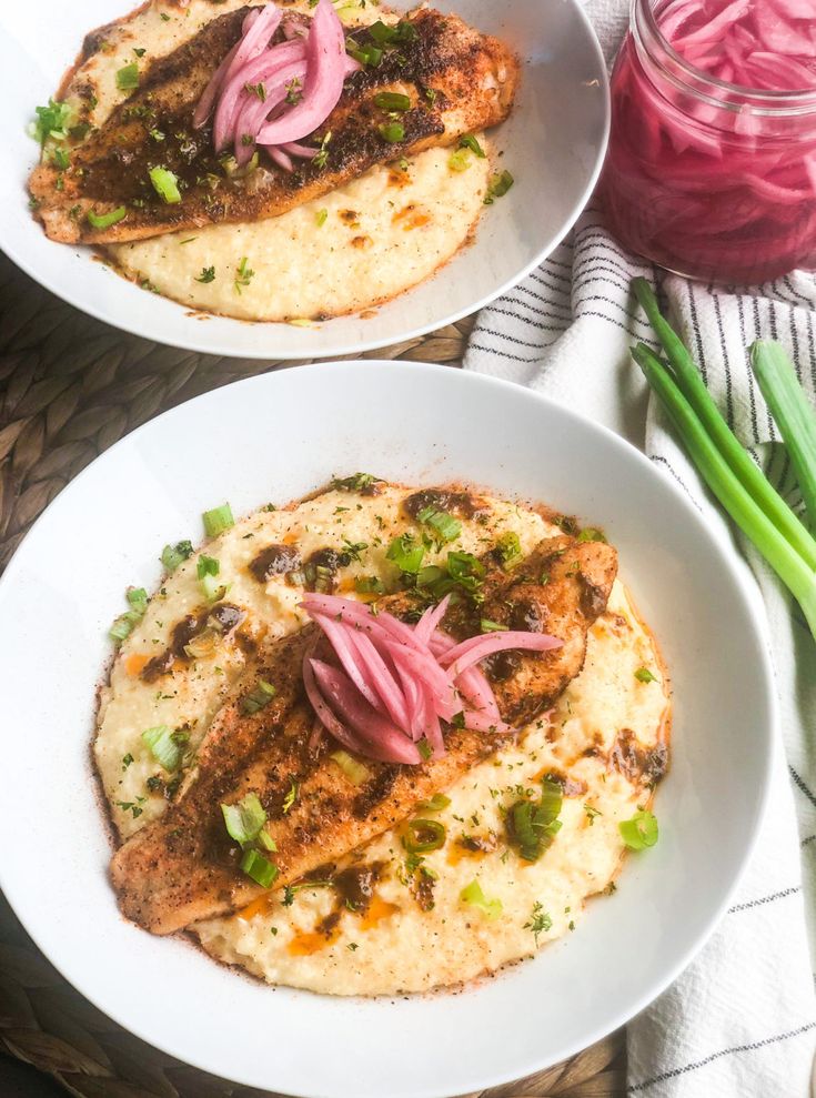 two white plates topped with food on top of a wooden table next to green onions