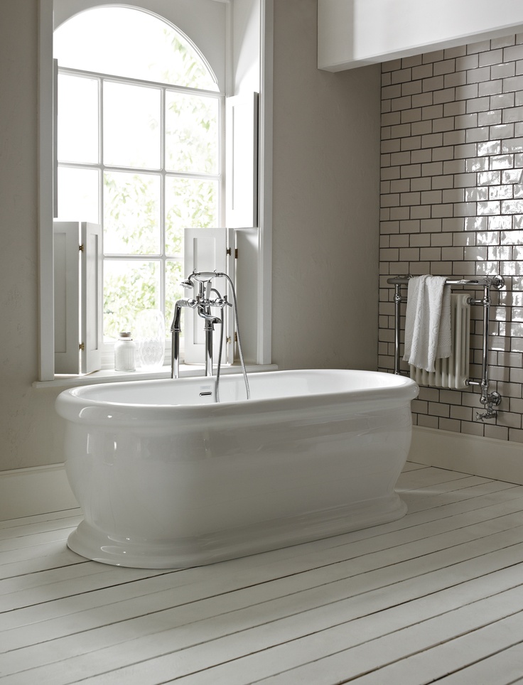 a large white bath tub sitting in a bathroom next to a window and tiled walls