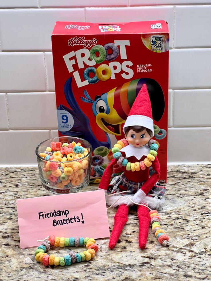 an elf is sitting on the counter next to some candy and a box of froot loops