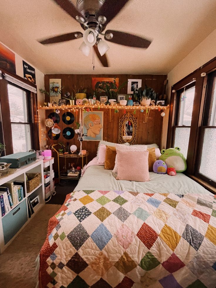 a bed room with a neatly made bed next to two windows and a ceiling fan