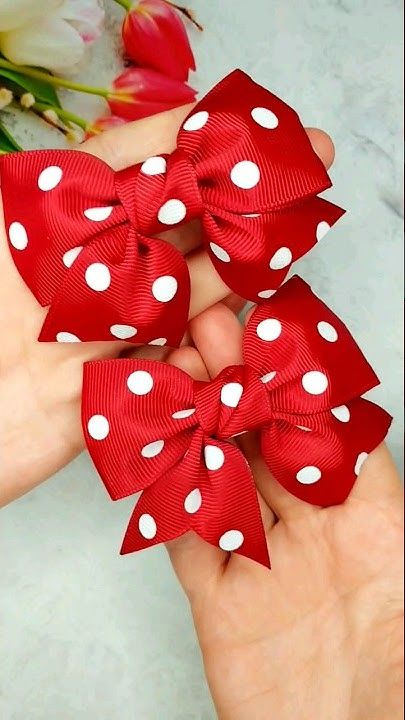 three red and white polka dot hair bows on someone's hand with flowers in the background