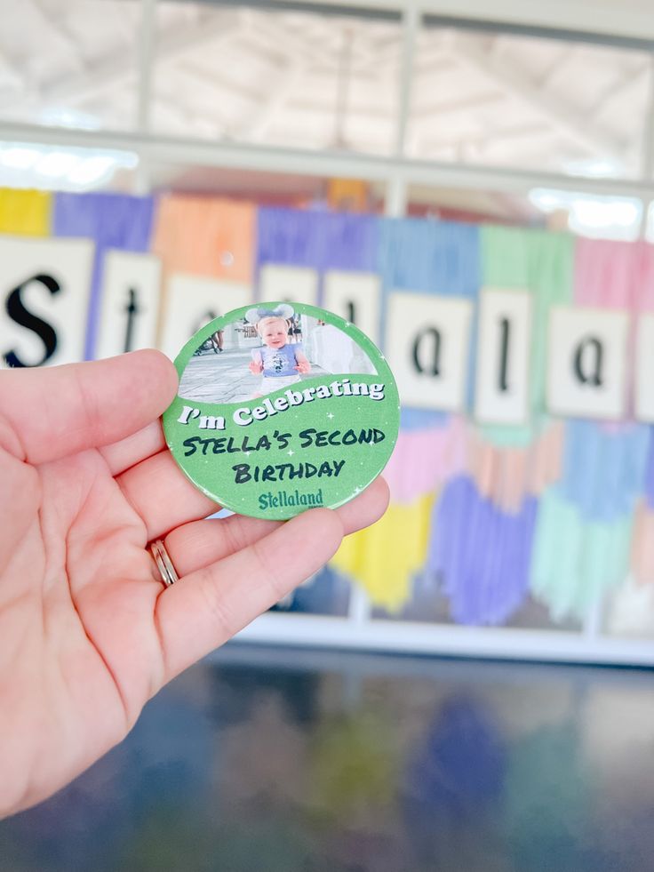 a person holding up a small green sticker that says i am celebrating stella's sesame birthday