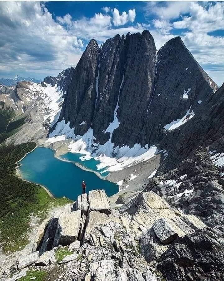 a man standing on top of a mountain next to a lake