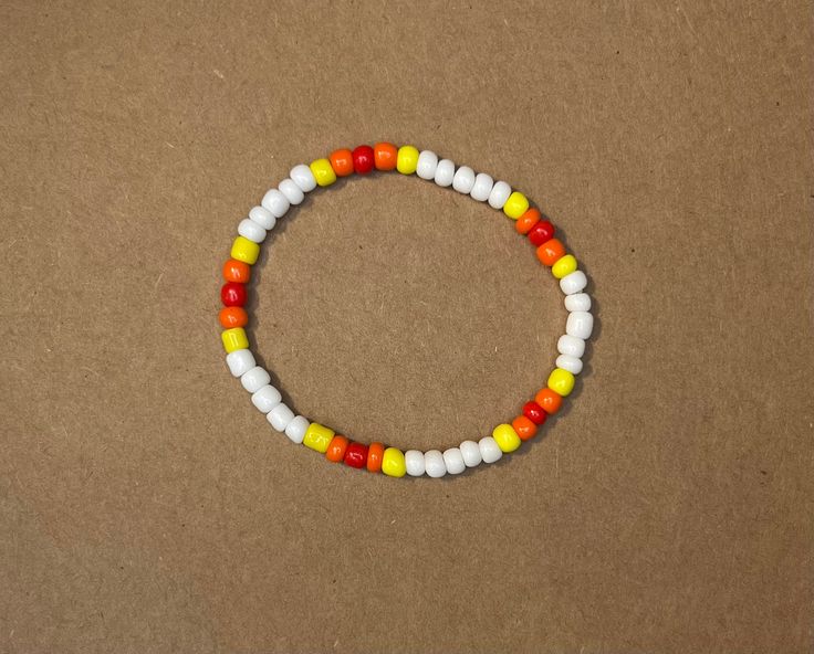 a beaded bracelet with white, yellow and red beads sits on a brown surface