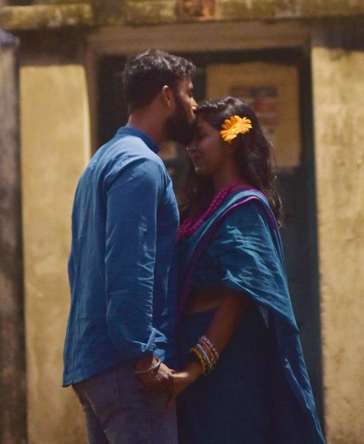 a man and woman standing next to each other in front of a building with a flower in their hair