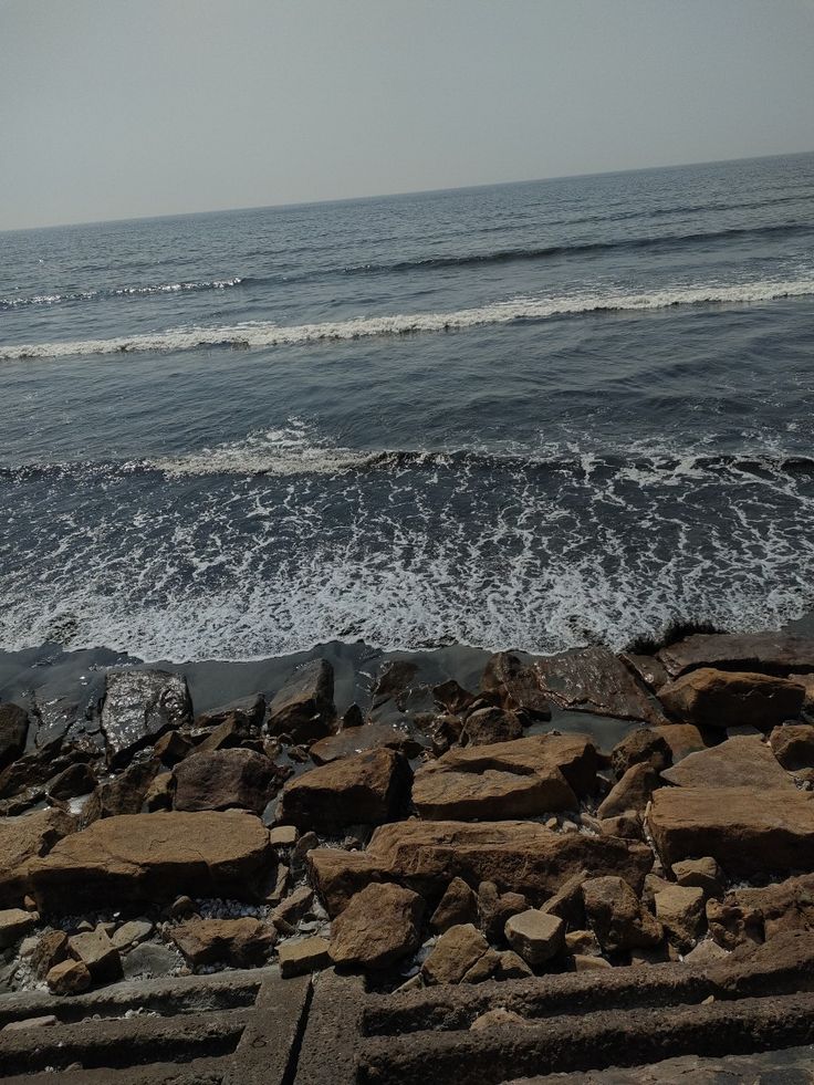 there is a bench sitting on the edge of rocks by the water's edge