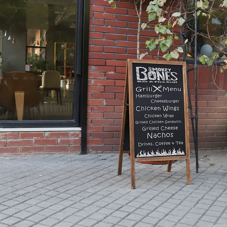 a menu board sitting on the sidewalk in front of a brick building with tables and chairs