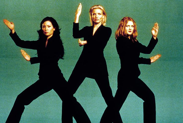 three women in black outfits are dancing against a green background with their hands up to the side