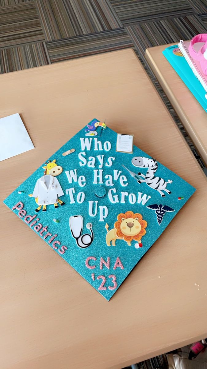 a blue graduation cap that says who says we have to grow up on a desk