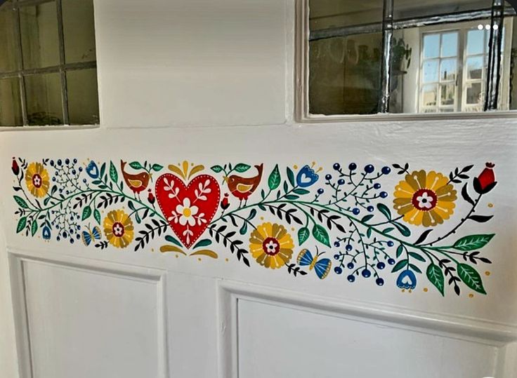 a painted door with flowers and birds on it's side, next to a window