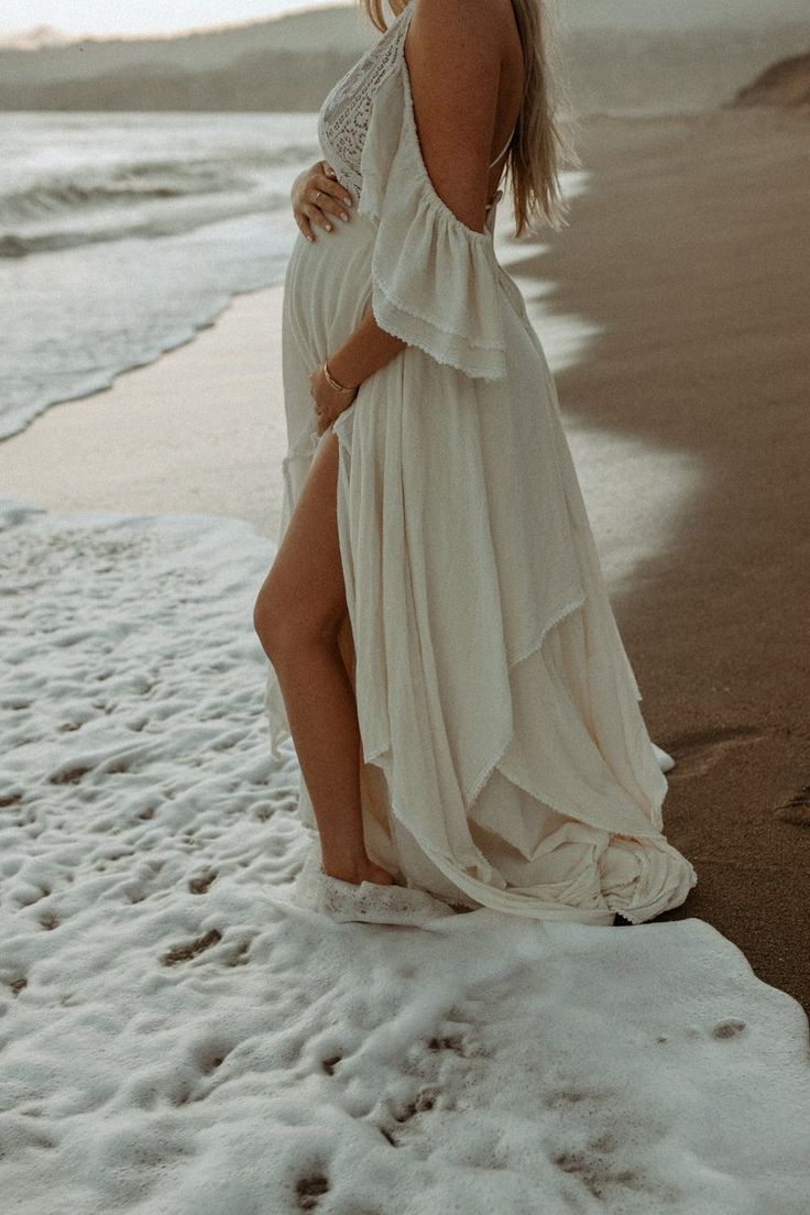 a pregnant woman in a white dress standing on the beach