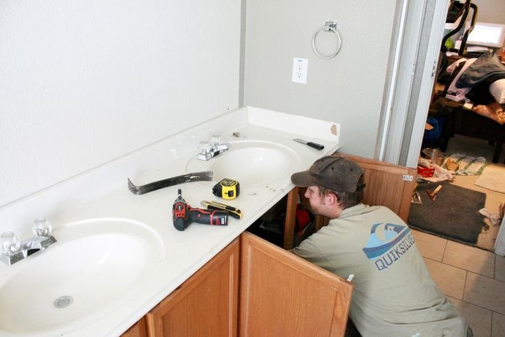 a man fixing a bathroom sink in front of a mirror with tools on the counter