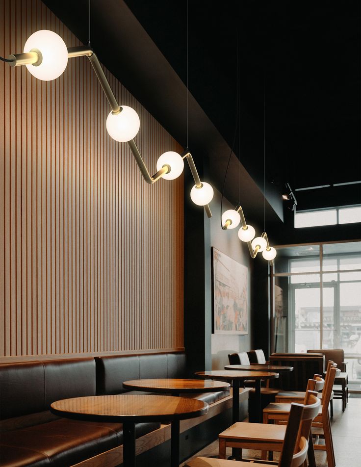 an empty restaurant with wooden tables and chairs in front of the window, along with hanging lights