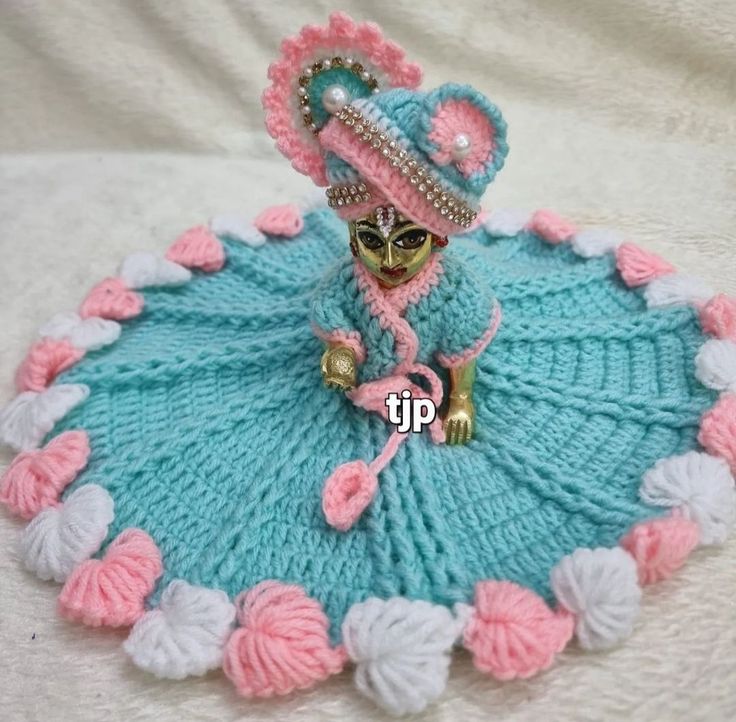 a crocheted doll sitting on top of a blue and white blanket with pink flowers