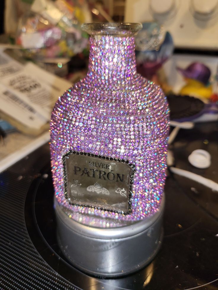 a bottle covered in lots of purple and silver glitter sitting on top of a table