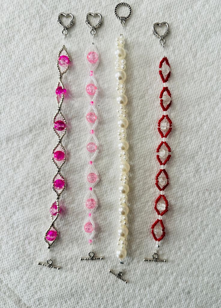 four different types of beaded bracelets on a white surface with two hearts hanging from them