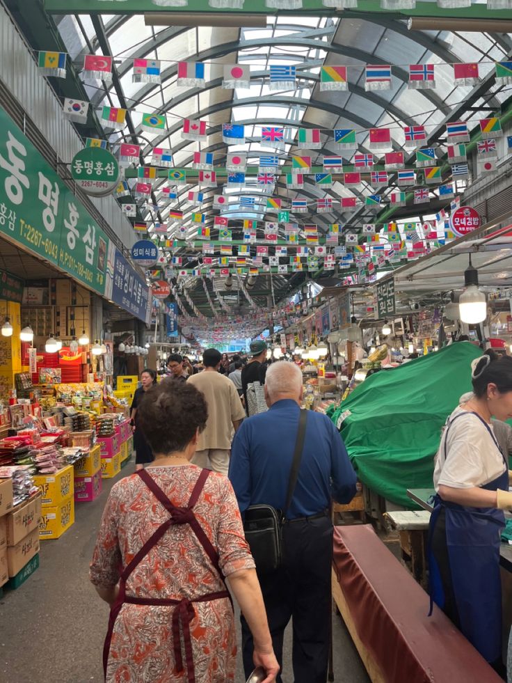 people are shopping in an indoor market with flags hanging from the ceiling