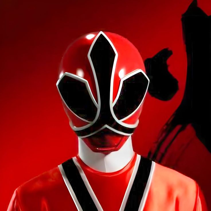 a person wearing a red and black mask with one hand up in the air while standing against a red background