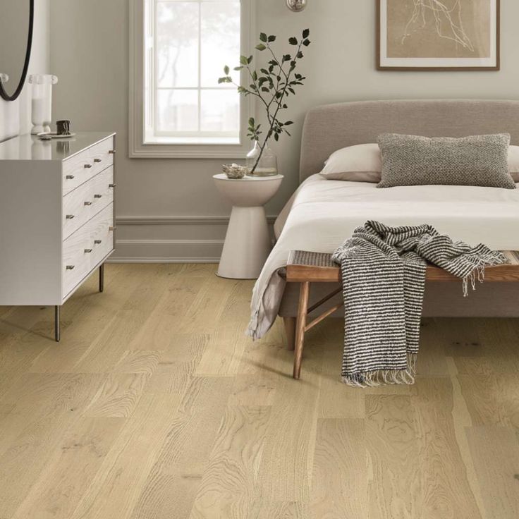 a bedroom with light wood floors and white furniture, including a large bed in the center