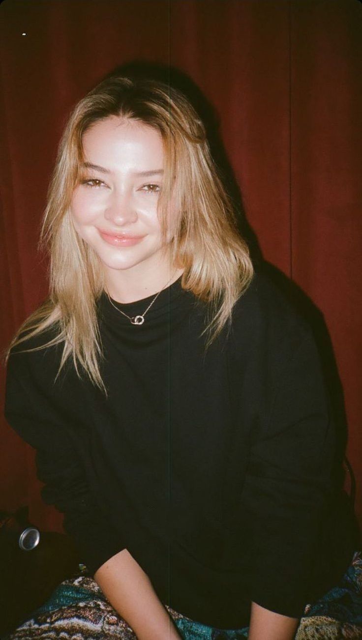 a young woman sitting on top of a bed next to a red curtain and smiling