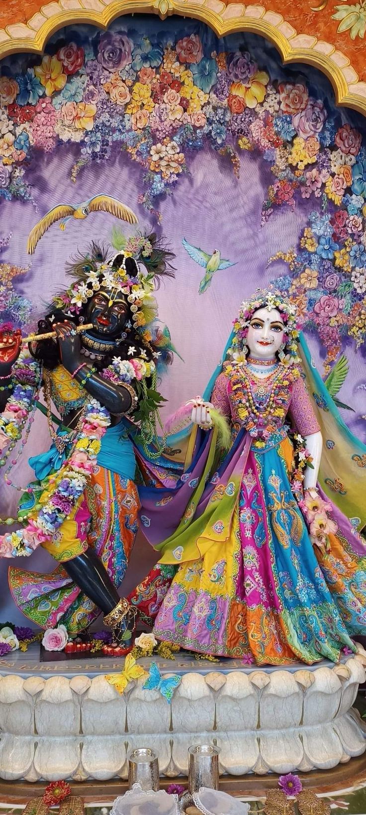 two people dressed in colorful costumes standing next to each other near a wall with flowers