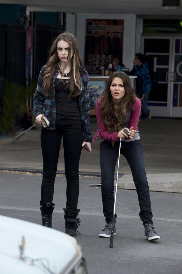 two girls on roller skates in the street with one holding a cane and another looking at something