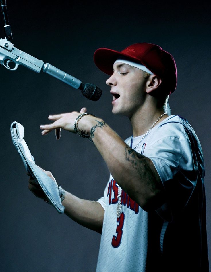 a young man singing into a microphone with his hands out to the side, while wearing a baseball cap