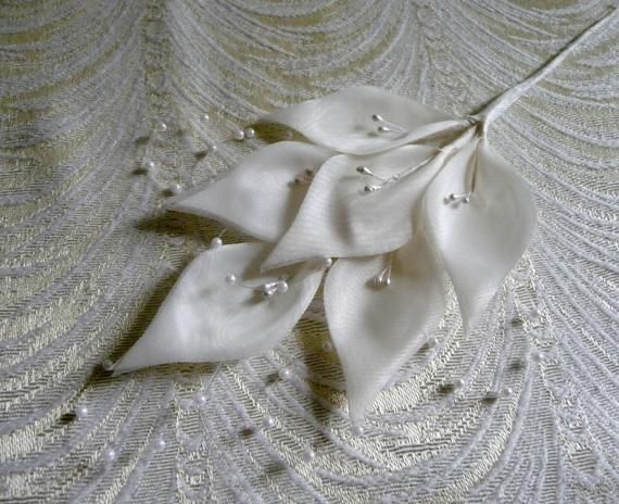 a white flower with pearls on it laying on a lace covered table cloth, next to a heart