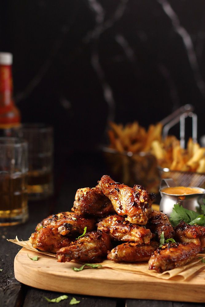 chicken wings on a cutting board with dipping sauces and other foods in the background